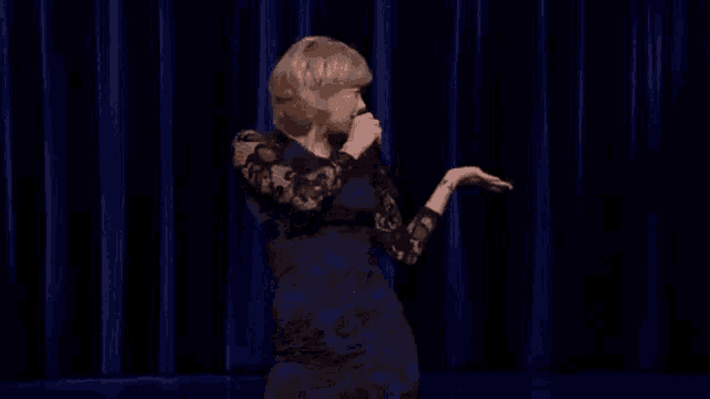 a woman in a blue dress is singing into a microphone on a stage in front of a blue curtain .