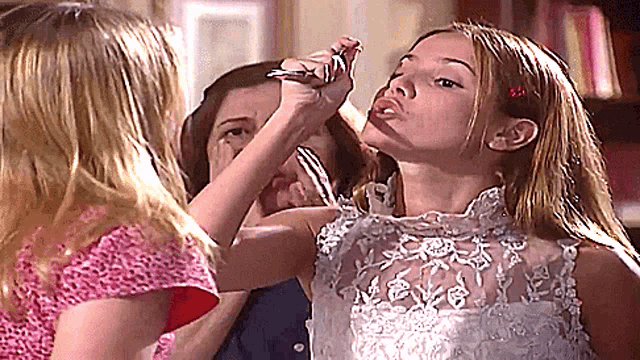 a girl in a white lace dress is being held by a woman in a pink shirt