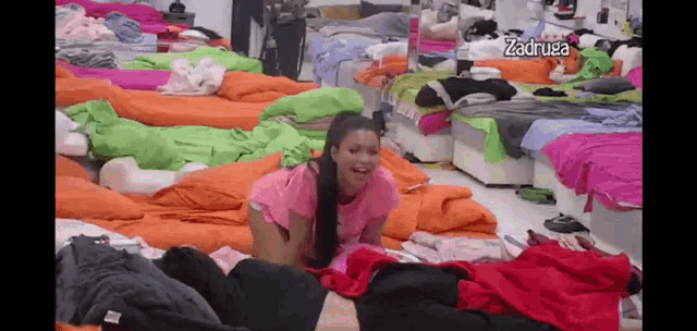 a woman in a pink shirt is laying on the floor in a room filled with lots of beds .