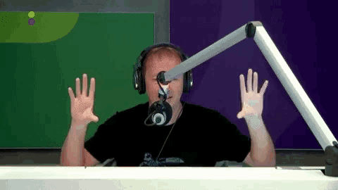 a man wearing headphones stands in front of a microphone with his hands in the air
