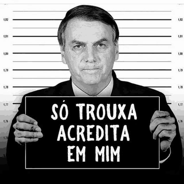 a man in a suit holds a sign that says so trouxa acredita em mim