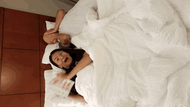 a man and a woman are laying on a bed under a blanket