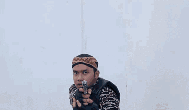 a man is pointing a gun at the camera while wearing a headband and gloves .