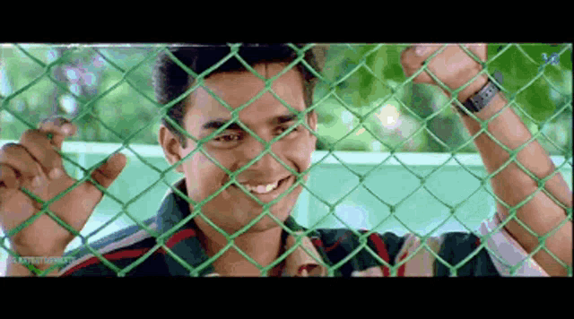 a man is smiling behind a chain link fence .