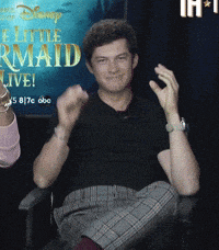 a man sitting in front of a sign that says ' the little mermaid live '