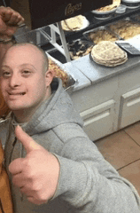 a man in a grey hoodie is giving a thumbs up in front of a coca cola sign