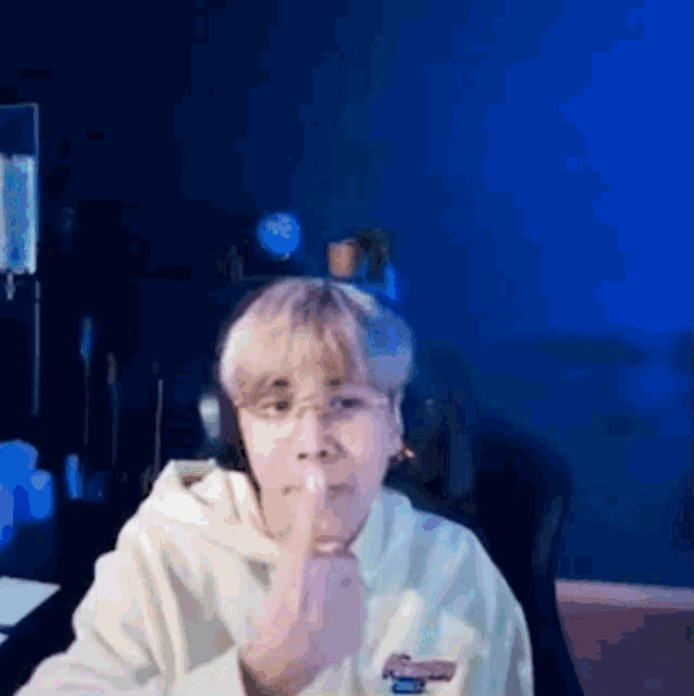 a man wearing headphones and a white hoodie is sitting in front of a blue wall and making a funny face .