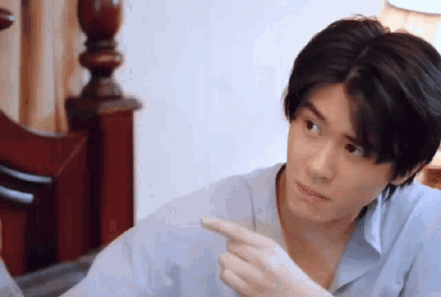 a young man is sitting on a bed and pointing at something .