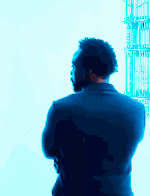 a man in a suit stands with his arms crossed in front of a blue background