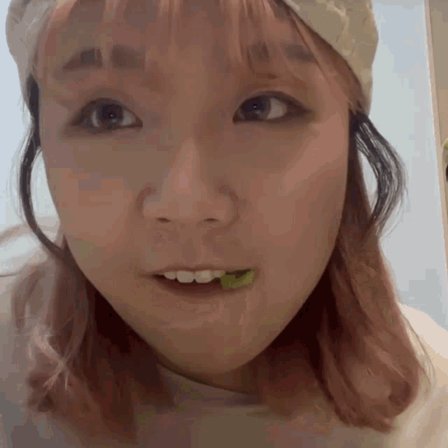 a woman with pink hair is eating a green leaf
