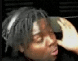 a man with dreadlocks is holding his hand to his forehead and making a funny face .