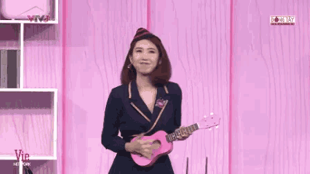 a woman is holding a pink ukulele in front of a pink wall with viet network written on it