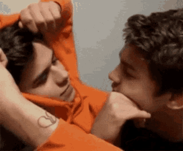 two young men are kissing each other while one of them has a tattoo on his arm .