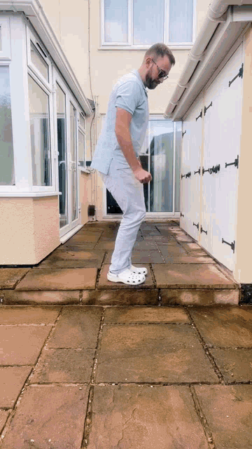 a man wearing a blue shirt and white crocs stands on a patio