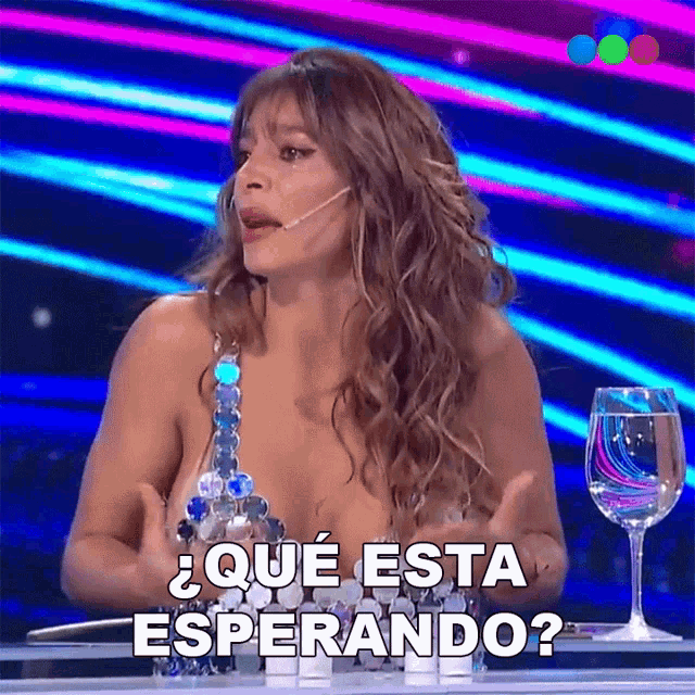 a woman sitting at a table with a glass of water and the words que esta esperando on the screen
