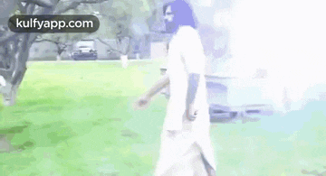 a man with a beard is walking through a grassy field in a park .