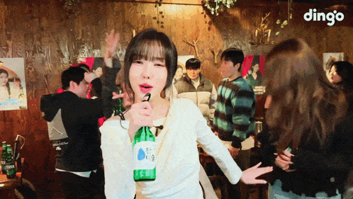 a woman is holding a bottle of beer in front of a group of people and the word dingo is on the bottom