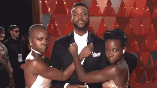 a man in a tuxedo has two women standing around him