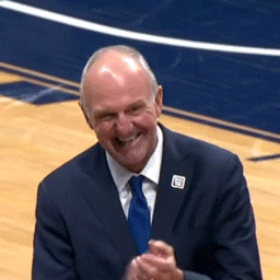 a man in a suit and tie is smiling and clapping on a basketball court