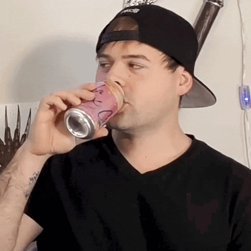 a man wearing a black hat is drinking from a can with a smiley face on it