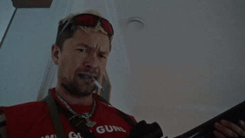 a man is holding a gun and wearing a red shirt that says wig gun