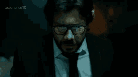 a man with a beard wearing glasses and a suit and tie is standing in a dark room .
