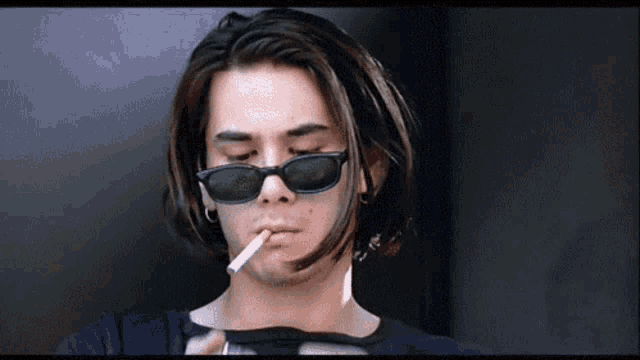 a man wearing sunglasses is lighting a cigarette