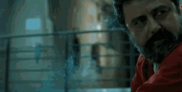 a man with a beard is wearing a red jumpsuit and looking at the camera .