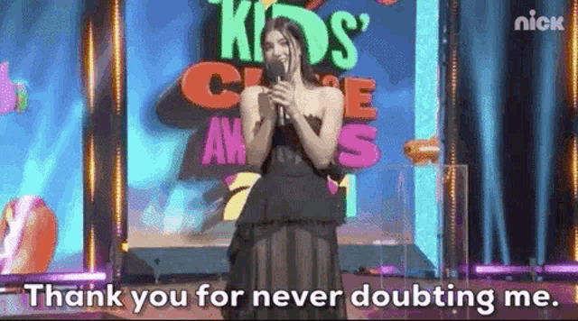 a woman in a black dress is standing on a stage holding a microphone and says thank you for never doubting me .