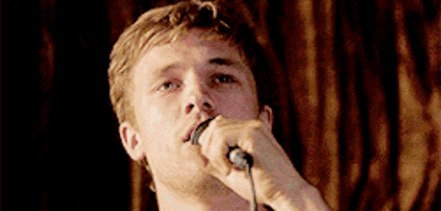 a man singing into a microphone with a brown curtain in the background