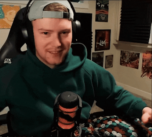 a man wearing headphones and a green hoodie is sitting in front of a microphone that says dx on it
