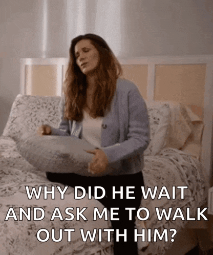 a woman sitting on a bed holding a pillow and asking why did he wait and ask me to walk out with him