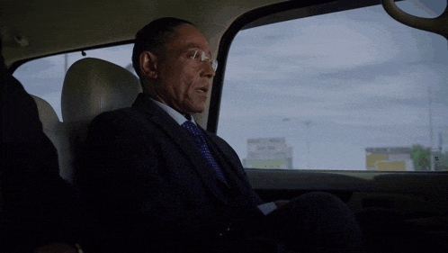 a man in a suit and tie sits in the back seat of a car and says can i see it