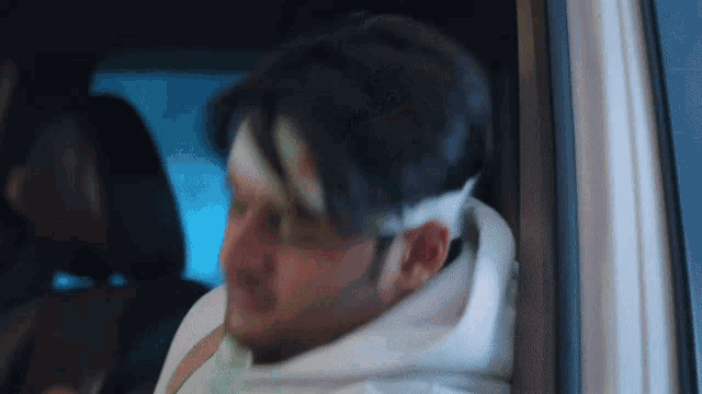 a man with a bandage on his head looks out of a car window