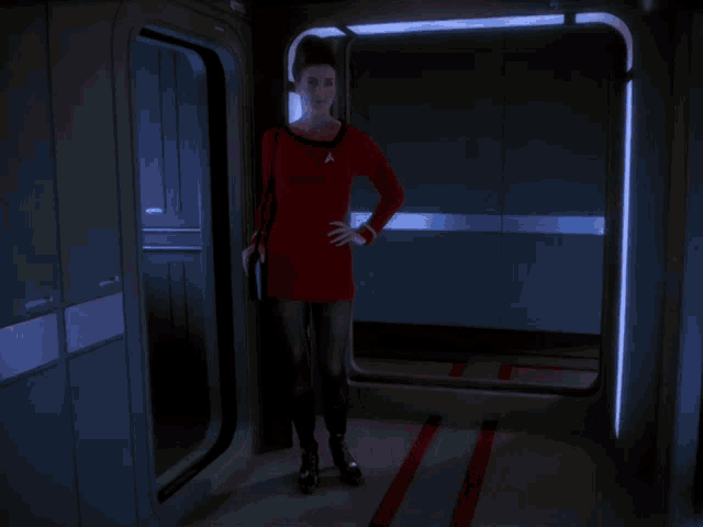 a woman in a red dress and black boots stands in a dark hallway