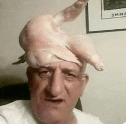 a man with a chicken on his head is taking a selfie .