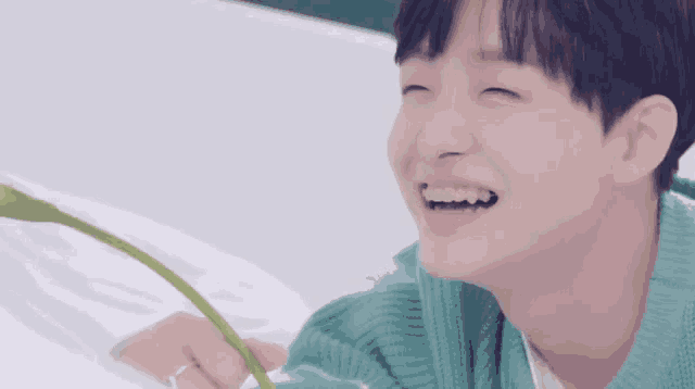 a young man in a blue sweater is smiling and holding a green flower