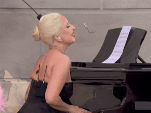 lady gaga is singing while playing a piano with sheet music on it