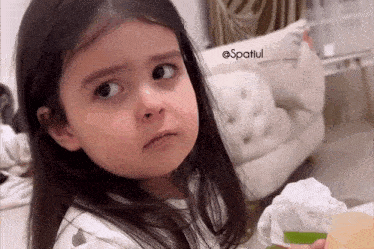 a little girl is making a funny face while sitting on a bed .