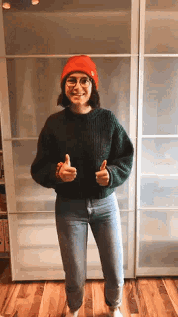 a woman wearing a green sweater and a red hat is giving two thumbs up .