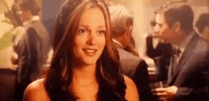 a woman in a black dress is smiling at the camera while standing in front of a crowd of people .