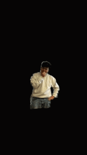 a young boy in a white sweater and blue jeans is standing in front of a black background
