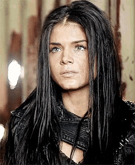 a woman with long black hair and blue eyes is wearing a leather jacket and looking at the camera .