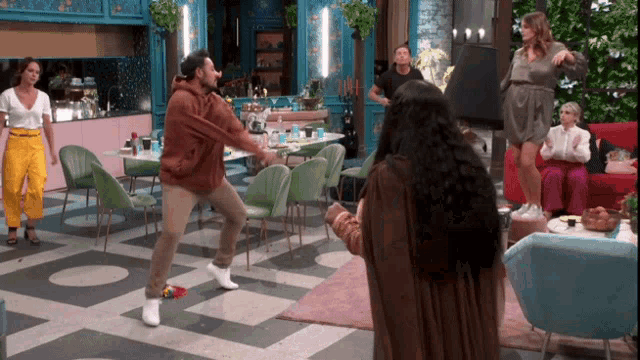 a group of people are dancing in a room including a man in a brown hoodie