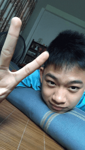 a young boy laying on a blue pillow giving the peace sign
