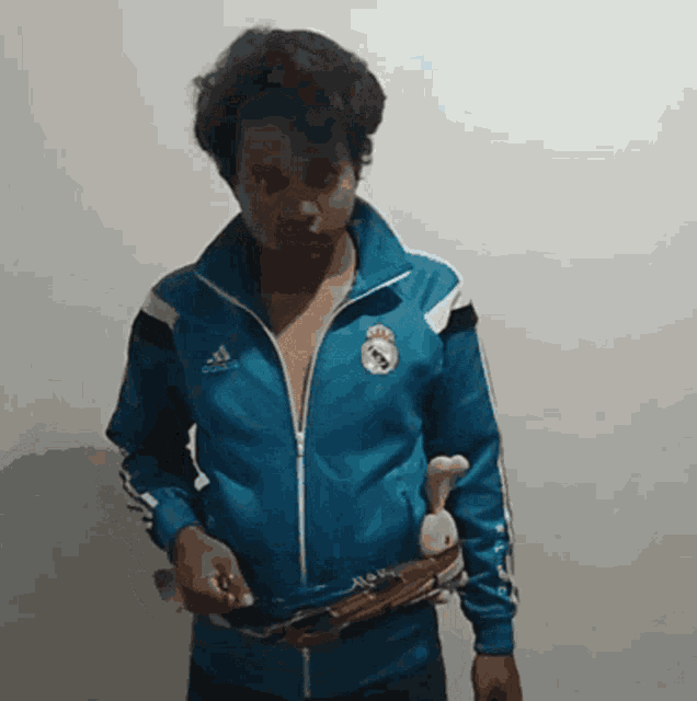 a man wearing a blue adidas jacket holds a toy