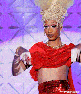 a drag queen wearing a red top and white gloves is dancing on a stage .