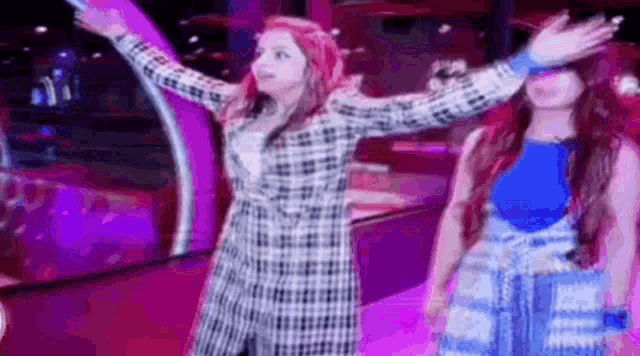 two women are standing next to each other with their arms outstretched in a room .