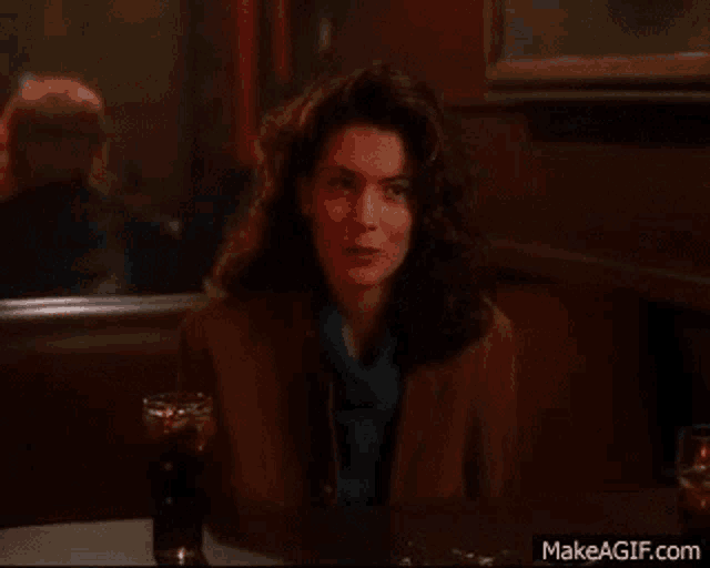 a woman is sitting at a table in a diner with a drink in her hand .