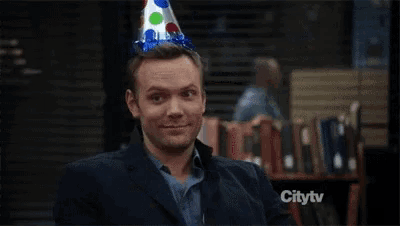 a man wearing a party hat is sitting at a table with a birthday cake